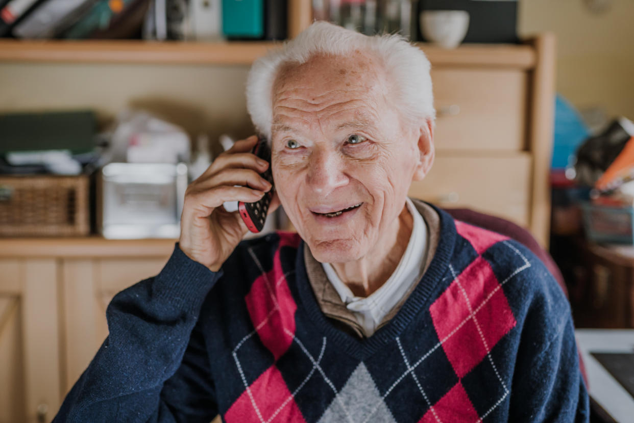 Old man using phone sitting at desk. Order food home with delivery, shopping ordered by phone. Phone call from family. Medical consultations by phone. Quarantine during virus Covid-19 pandemic.