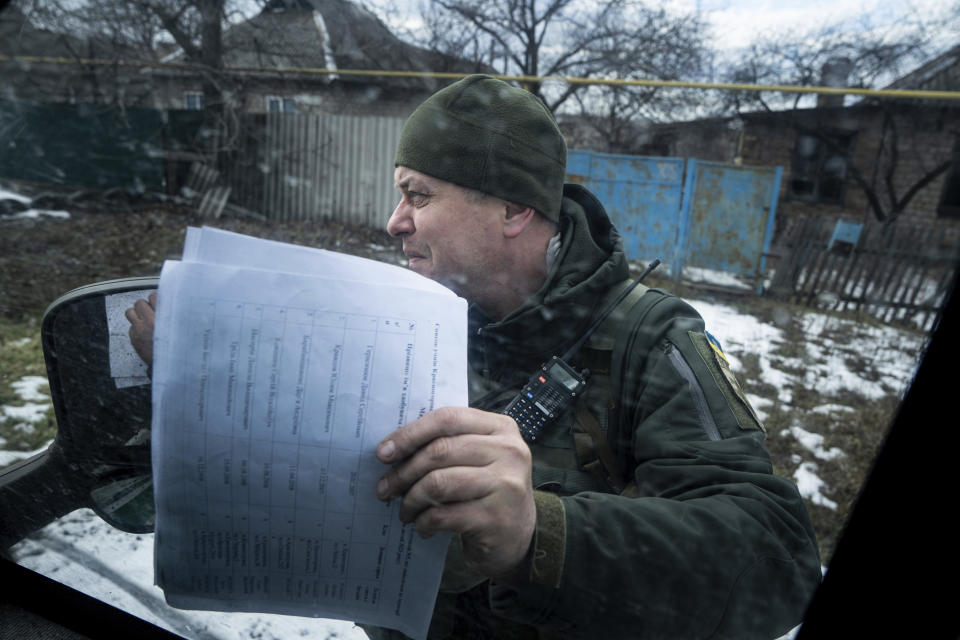A Ukrainian police officer of the White Angels unit, checks the list of families with children which they need to visit, in Krasnohorivka, Ukraine, Tuesday, Feb. 21, 2023. A special unit known as the White Angels risk their lives to head into front-line villages and towns, knocking on doors and pleading with the few remaining residents to evacuate. (AP Photo/Evgeniy Maloletka)