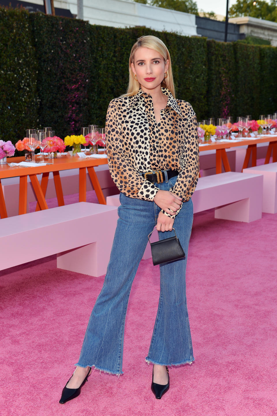 Emma poses for a photo at an event while wearing jeans, a long-sleeved blouse and kitten slingback heels