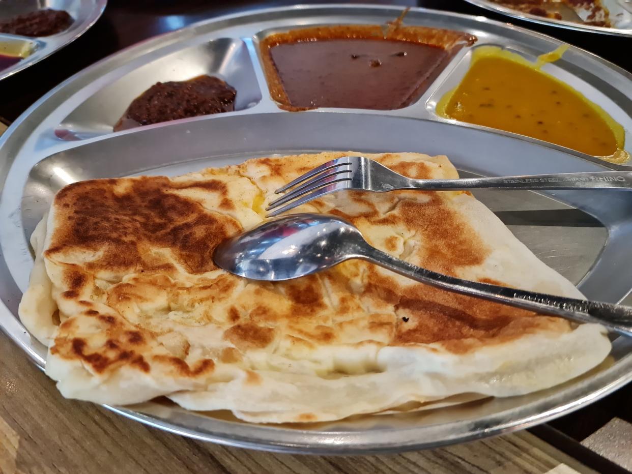 Roti canai or roti prata on a plate with curry and chilli.