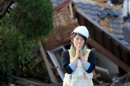 A woman reacts in front of collapsed house caused by an earthquake in Mashiki town, Kumamoto prefecture, southern Japan, in this photo taken by Kyodo April 16, 2016. REUTERS/Kyodo