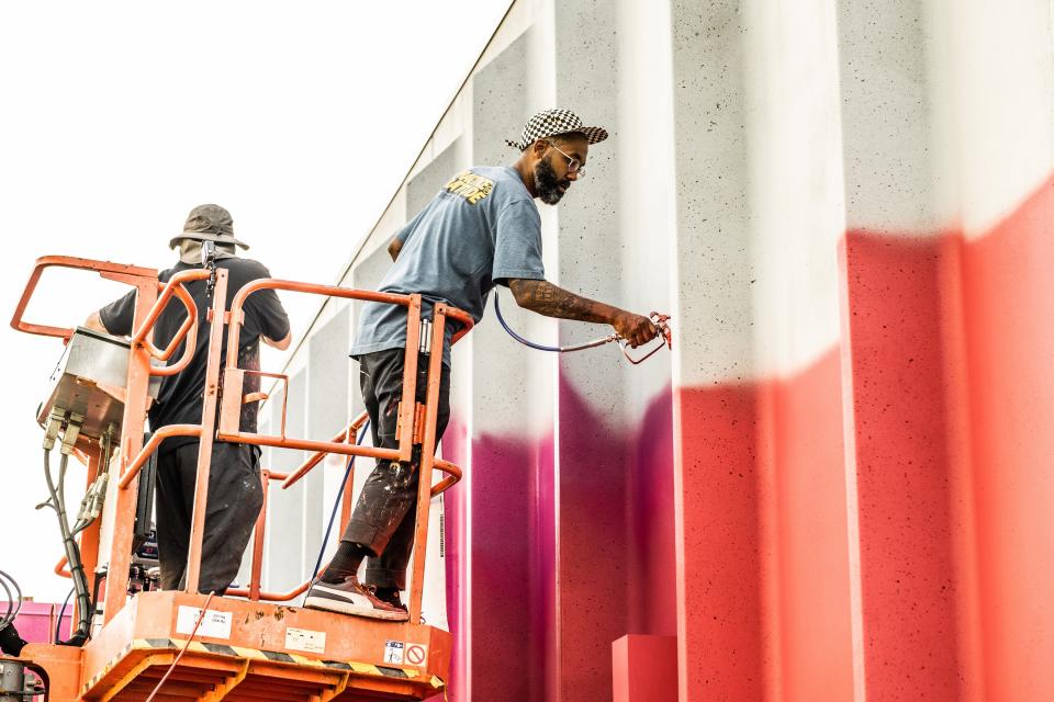 Detroit-based artist and entrepreneur Rick Williams (right) works on his mural with his friend Ghost Beard along the wall of Monroe Community Ambulance's station at East First Street and Conant Avenue in downtown Monroe.