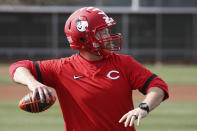 Cincinnati Reds strength coach Sean Marohn wears a football helmet as he throws a football to an outfielder as they warm up during baseball spring training Friday, Feb. 21, 2020, in Goodyear, Ariz. (AP Photo/Ross D. Franklin)