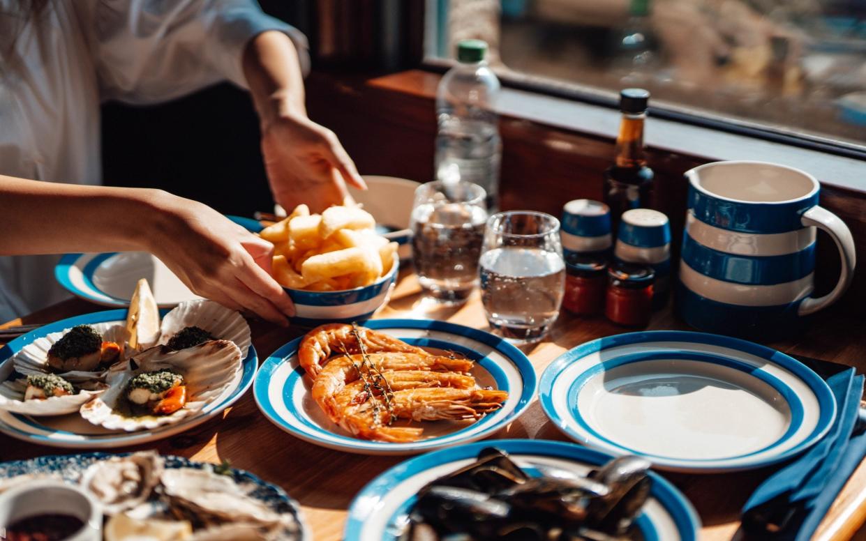 female hands passing a bowl of French fries, various seafood served on the dining table with beautiful sunlight