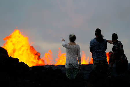 Onlookers stand on a lava flow to watch lava gush out of a fissure, in the Leilani Estates near Pahoa, Hawaii, U.S., May 26, 2018. REUTERS/Marco Garcia