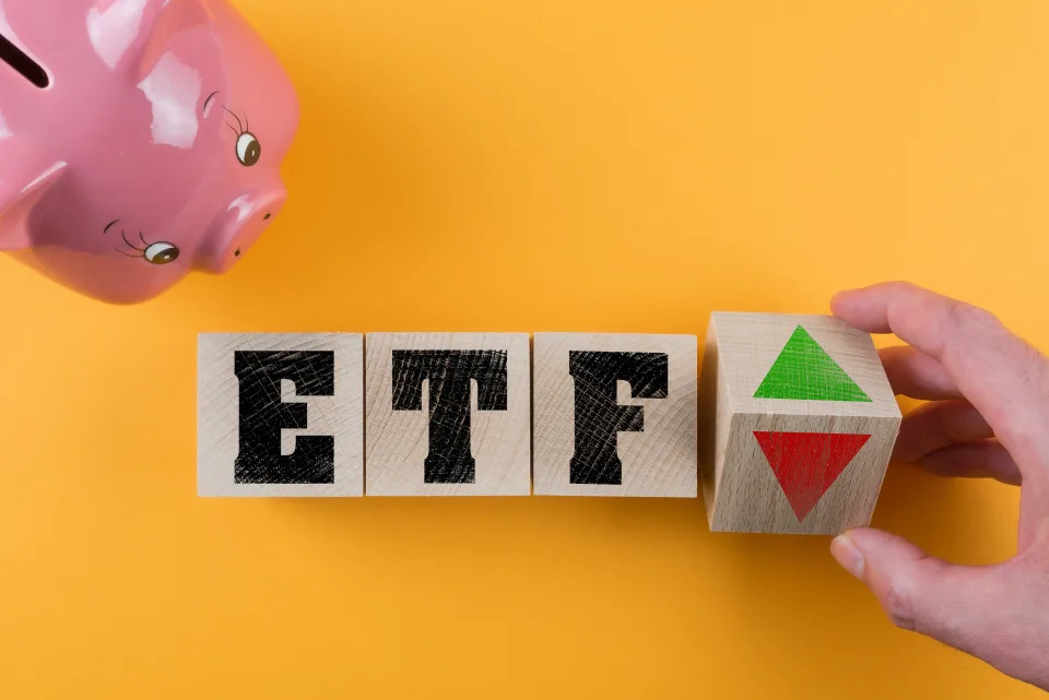 ETF exchange traded fund and red and green arrow symbol on wood cubes besides piggy bank on colored background, investing money concept