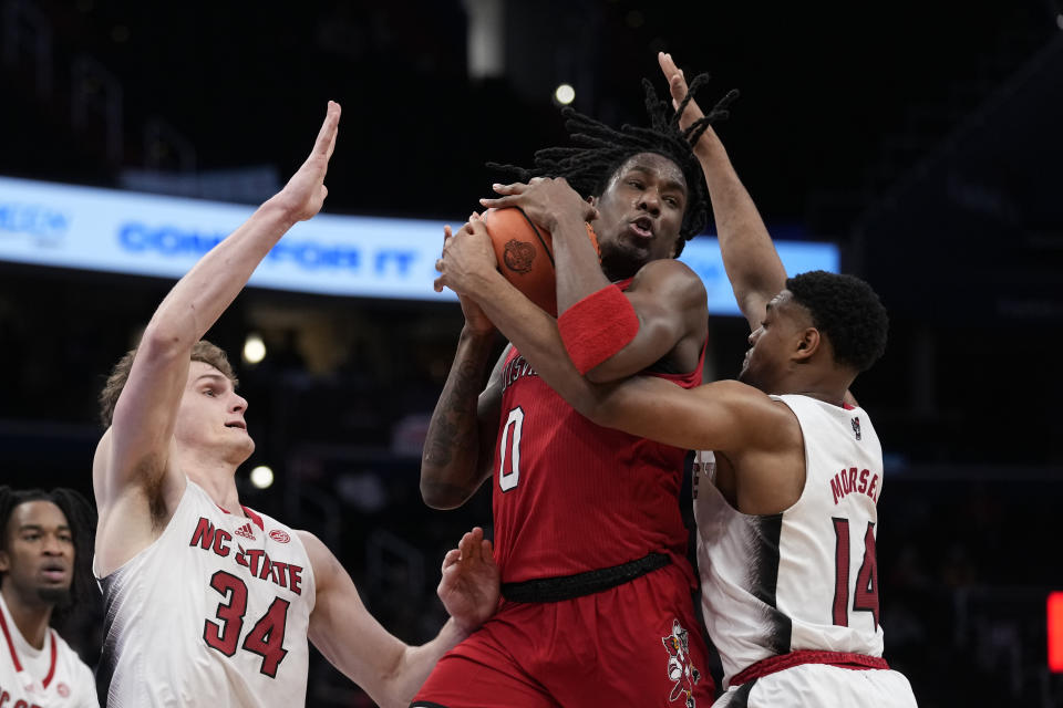 Louisville guard Mike James (0) rebounds the ball as he goes up against North Carolina State forward Ben Middlebrooks (34) and guard Casey Morsell (14) during the second half of the Atlantic Coast Conference NCAA college basketball tournament Tuesday, March 12, 2024, in Washington. (AP Photo/Susan Walsh)