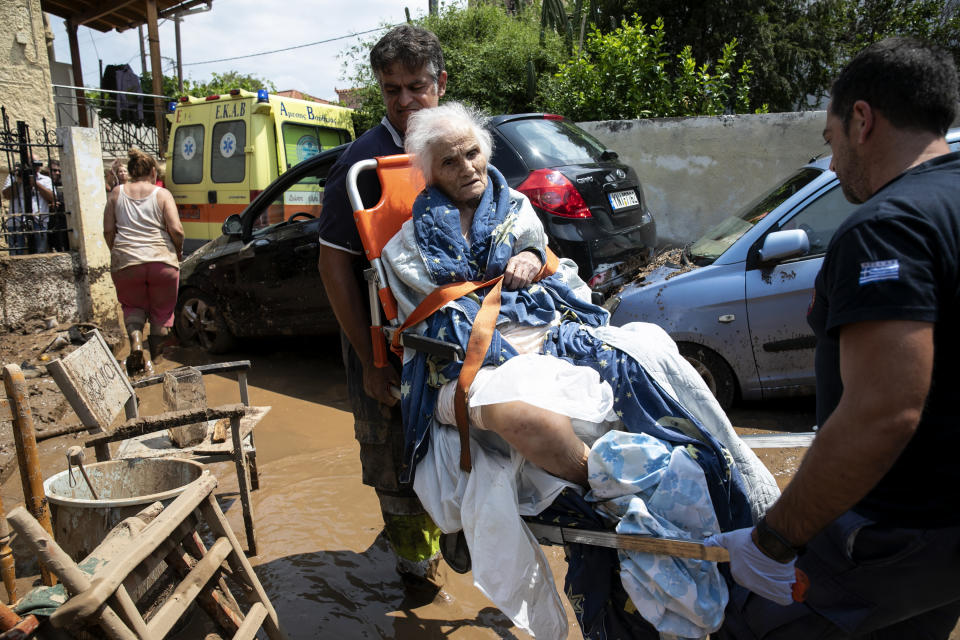 A woman is evacuated form her home by paramedics, following a storm at the village of Politika, on Evia island, northeast of Athens, on Sunday, Aug. 9, 2020. Five people have been found dead and dozens have been trapped in their homes and cars from a storm that has hit the island of Evia, in central Greece, police say. (AP Photo/Yorgos Karahalis)