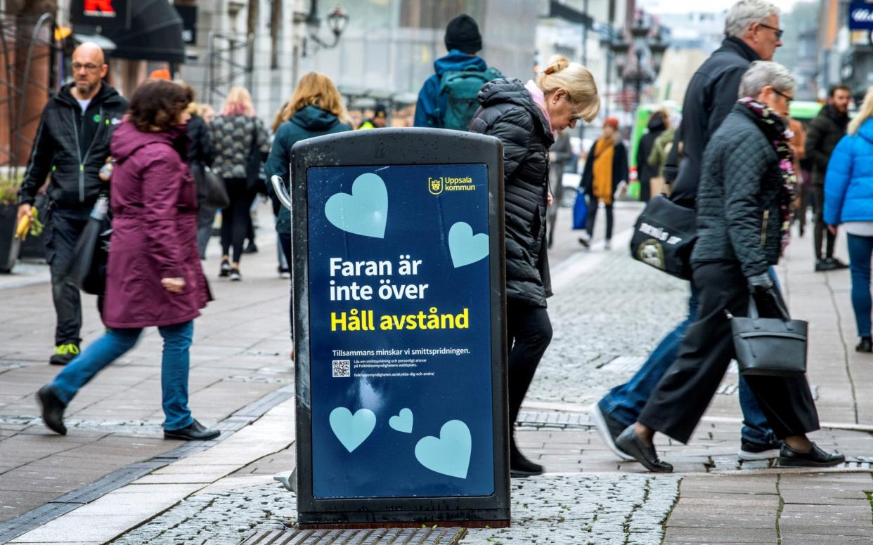 Pedestrians in Uppsala walk past a bin that carries a sign saying "the danger is not over - keep your distance" - TT News Agency/Claudio Bresciani via REUTERS