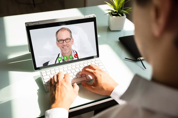 Man with hands on keyboard and doctor appearing on tablet screen