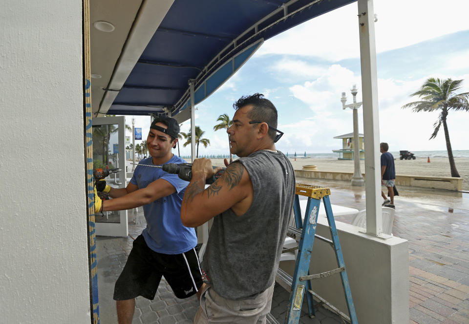 Workers Elmer Ramos, right, and Mariano Arzayus put plywood over the windows of the Yogurt Ur Way Cafe in preparation for Hurricane Dorian as the storm approaches the Florida coast on Saturday, Aug. 31, 2019 at Hollywood, Fla. The latest forecast says Hurricane Dorian is expected to stay just off shore of Florida and skirt the coast of Georgia, with the possibility of landfall still a threat on Wednesday, and then continuing up to South Carolina early Thursday. (David Santiago/Miami Herald via AP)