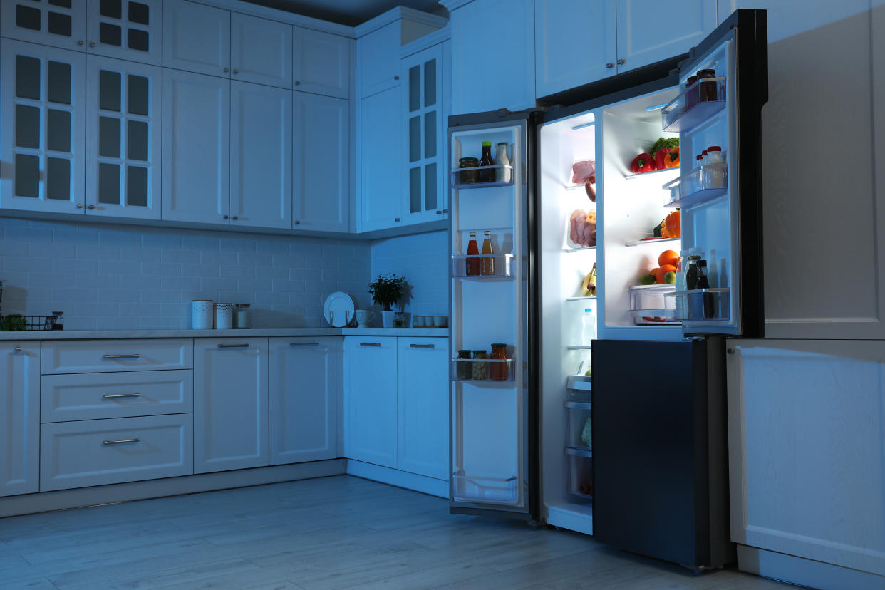 Open refrigerator filled with food in kitchen at night