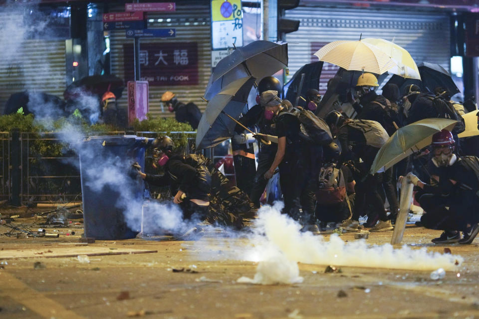 Protesters cover with umbrella as Police fire tear gas in the Kowloon area of Hong Kong, Monday, Nov. 18, 2019. As night fell in Hong Kong, police tightened a siege Monday at a university campus as hundreds of anti-government protesters trapped inside sought to escape. (AP Photo/Vincent Yu)