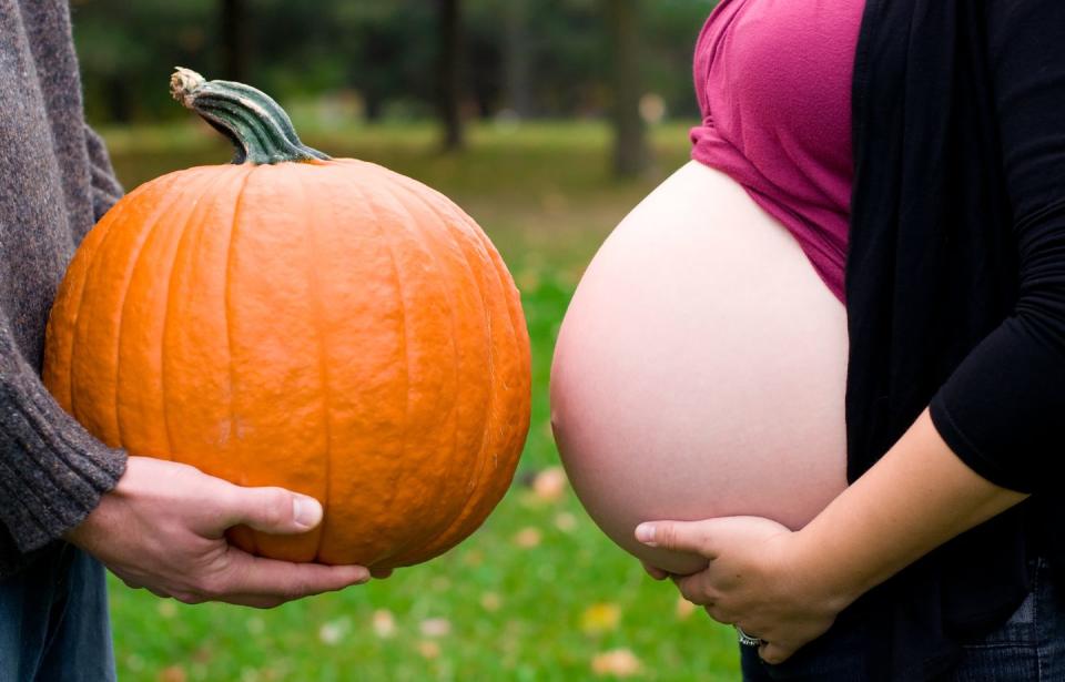 side view pregnant belly with bright orange pumpkin beside it