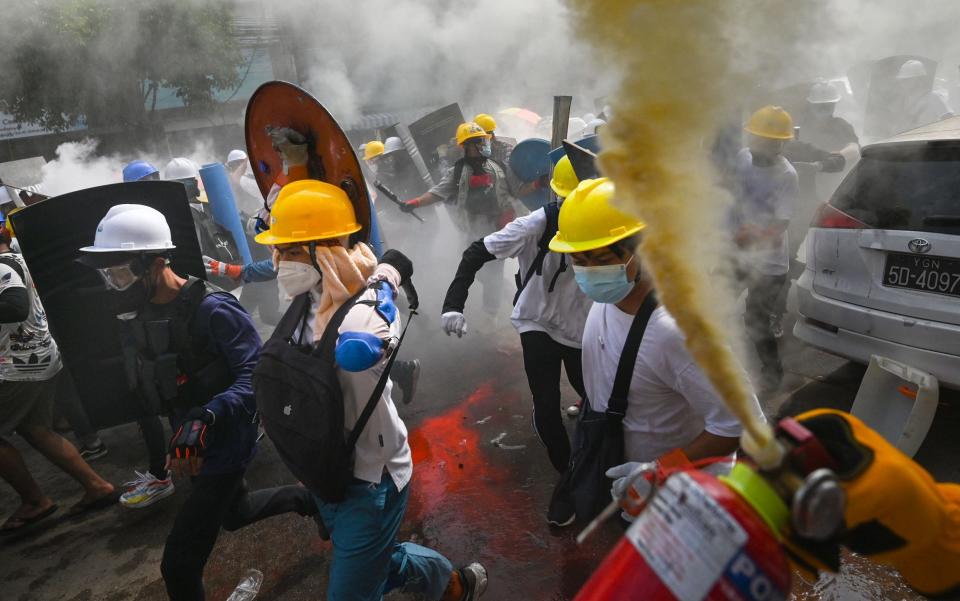 A protester uses a fire extinguisher as others holding homemade shields run during a demonstration - AFP