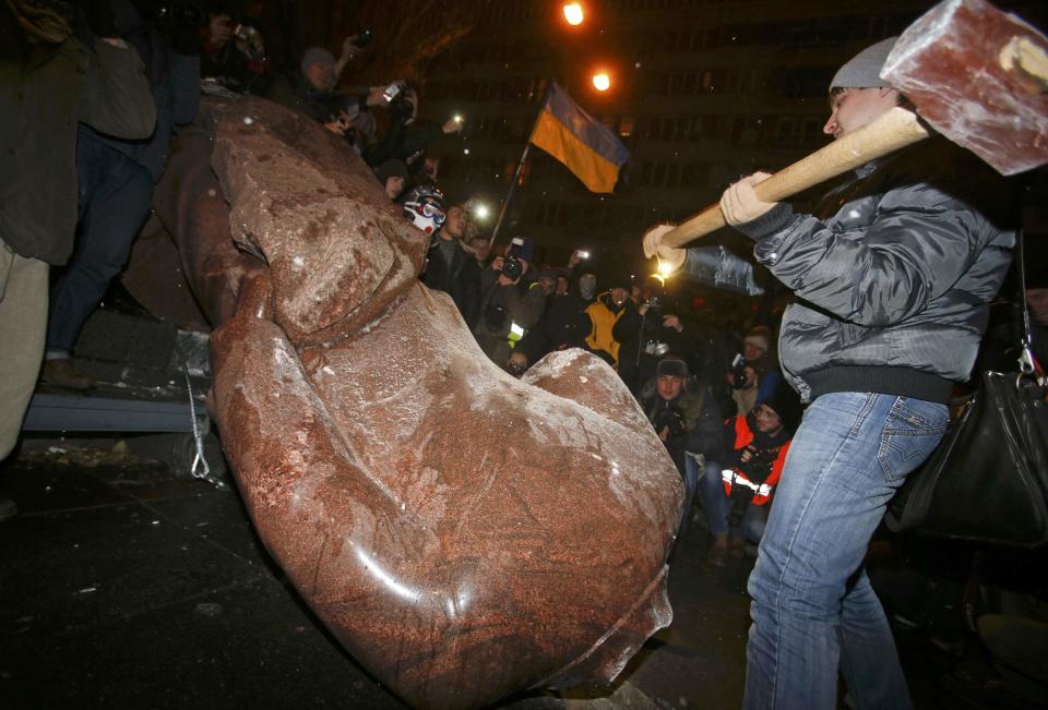 A man holds a sledgehammer as he smashes a statue of Soviet state founder Vladimir Lenin, which was toppled by protesters during a rally organized by supporters of EU integration in Kiev