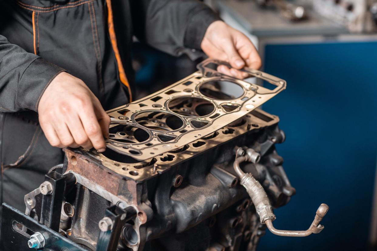 Sealing gasket in hand. The mechanic disassemble block engine vehicle. Engine on a repair stand with piston and connecting rod of automotive technology. Interior of a car repair shop