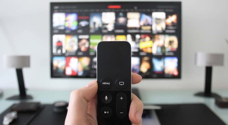 A close-up shot of a hand holding a TV remote with a blurred screen in the background.