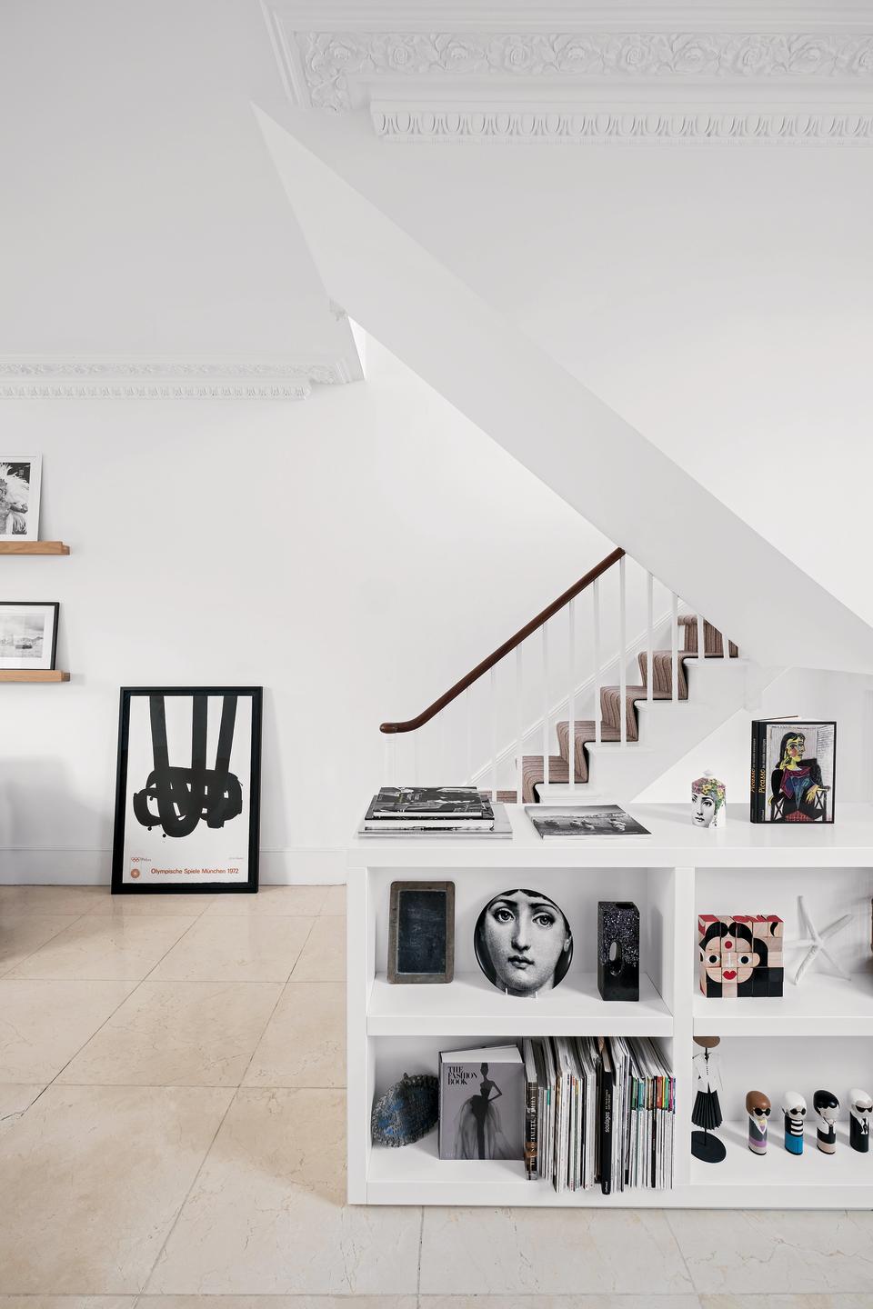 Hallway with tiled floor, white walls, carpeted staircase and shelving displaying books and ornaments.