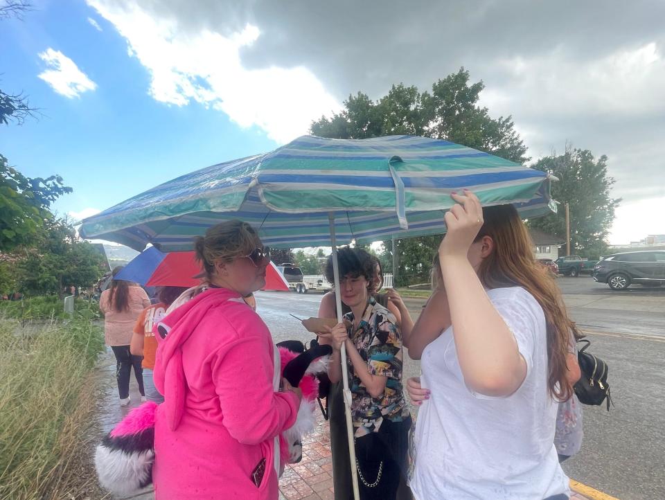 gray clouds above individuals holding a large umbrella in the rain as they wait in line for the Jeffree Star job