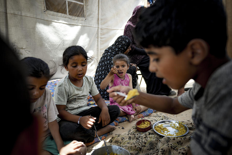 Members of the Al-Ashqar family, who were displaced by the Israeli bombardment of the Gaza Strip, eat lunch at a makeshift tent camp in Khan Younis, southern Gaza Strip, Thursday, July 4, 2024. Over nine months of war between Israel and Hamas, Palestinian families in Gaza have been uprooted repeatedly, driven back and forth across the territory to escape the fighting. Each time has meant a wrenching move to a new location and a series of crowded, temporary shelters. (AP Photo/Abdel Kareem Hana)