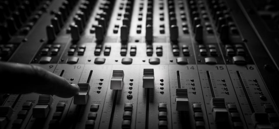 A close-up of a hand adjusting sliders on an audio mixing console, showing various levels and controls