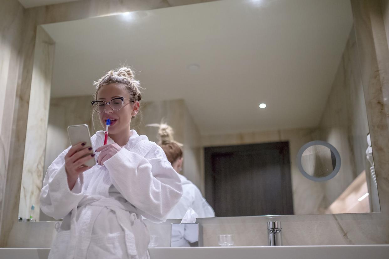 young woman brushing her teeth while texting