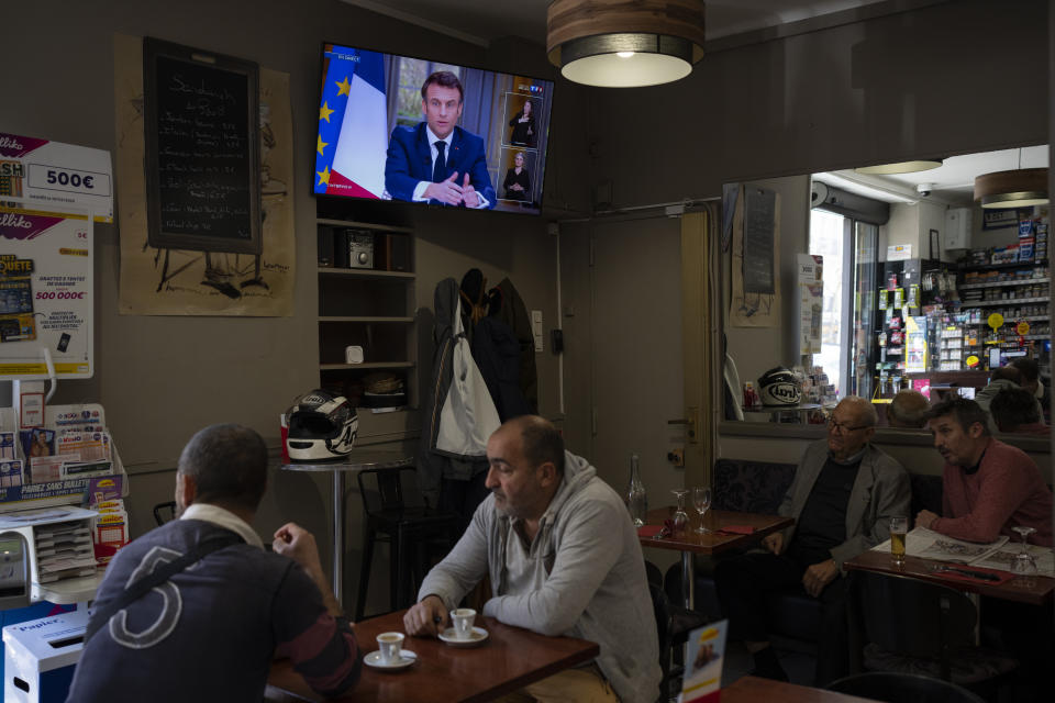 People sit at a bar while French President Emmanuel Macron speaks during an interview with journalists on television in Marseille, southern France, Wednesday, March 22, 2023. Macron said Wednesday that the pension bill that he pushed through without a vote in parliament needs to be implemented by the "end of the year.” (AP Photo/Daniel Cole)