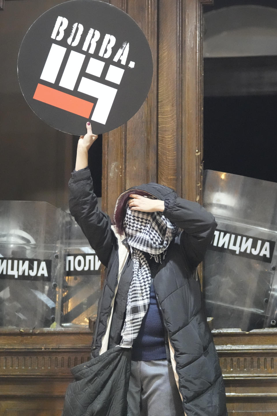 A protester holds a placard reading 'fight' at the entrance of city council building secured by anti-riot police in Belgrade, Serbia, Sunday, Dec. 24, 2023. Police in Serbia have fired tear gas to prevent hundreds of opposition supporters from entering the capital's city council building to protest what election observers said were widespread vote irregularities during a general election a week ago. (AP Photo/Darko Vojinovic)