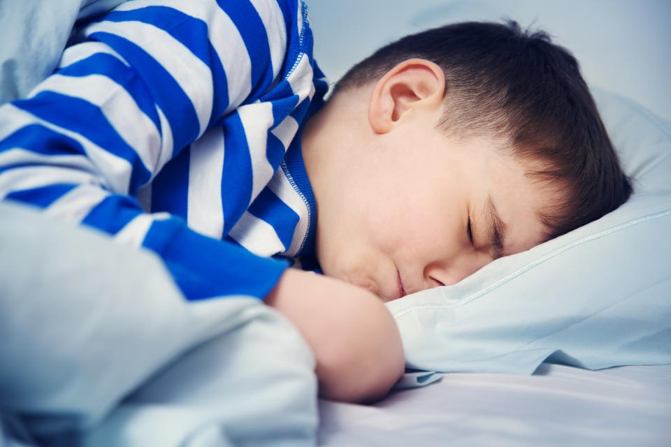 Boy sleeping in bed in pajamas. Child lying in bed on pillow at night.
