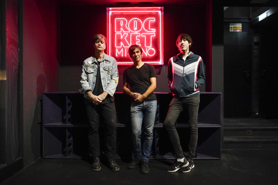 Francesco Orcese, known as Richey V, left, Massimiliano Ruffolo, owner of the Rocket Club, center, and Davide Volonte' stand next to a neon sign inside the empty venue, in Milan, Saturday, Sept. 25, 2021. With Italy’s vaccination campaign now advanced, the government has finally given the green light for nightclubs to reopen this weekend. It's been a long wait. They are recommending that venues can open at 50% capacity indoors, and 70% in the open air. (AP Photo/Alberto Pezzali)