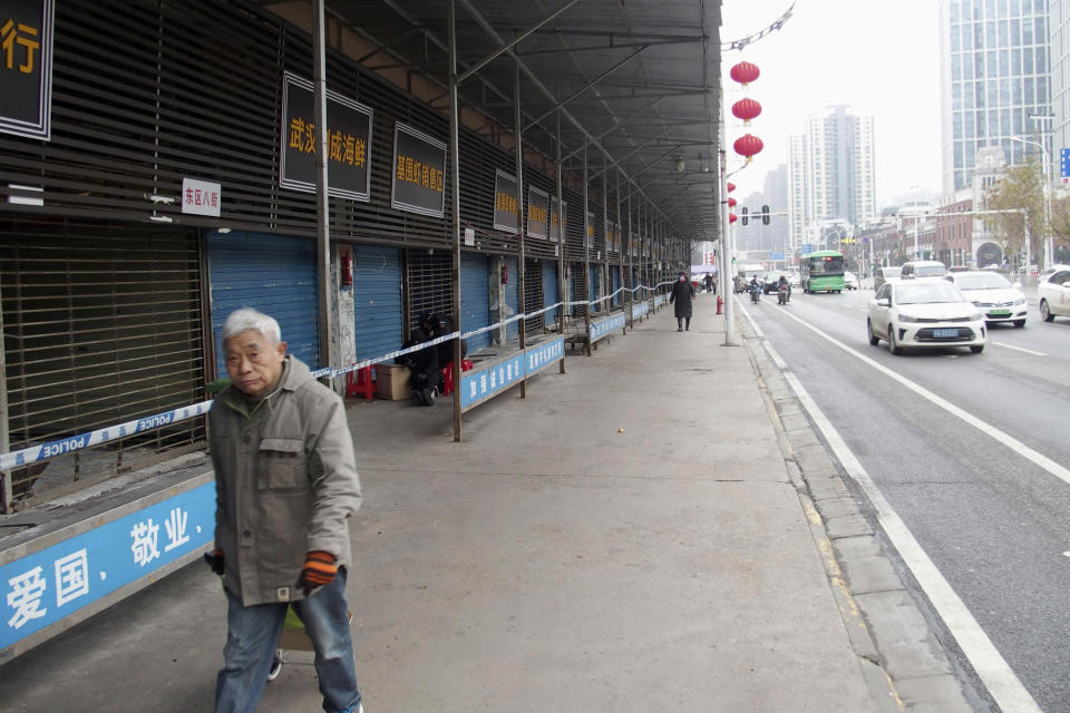 En la imagen del 17 de enero de 2020, un hombre pasa frente al Mercado Huanan de Mariscos, que permanece cerrado tras un brote de coronavirus ligado al lugar, en Wuhan, China. (Kyodo News vía AP)