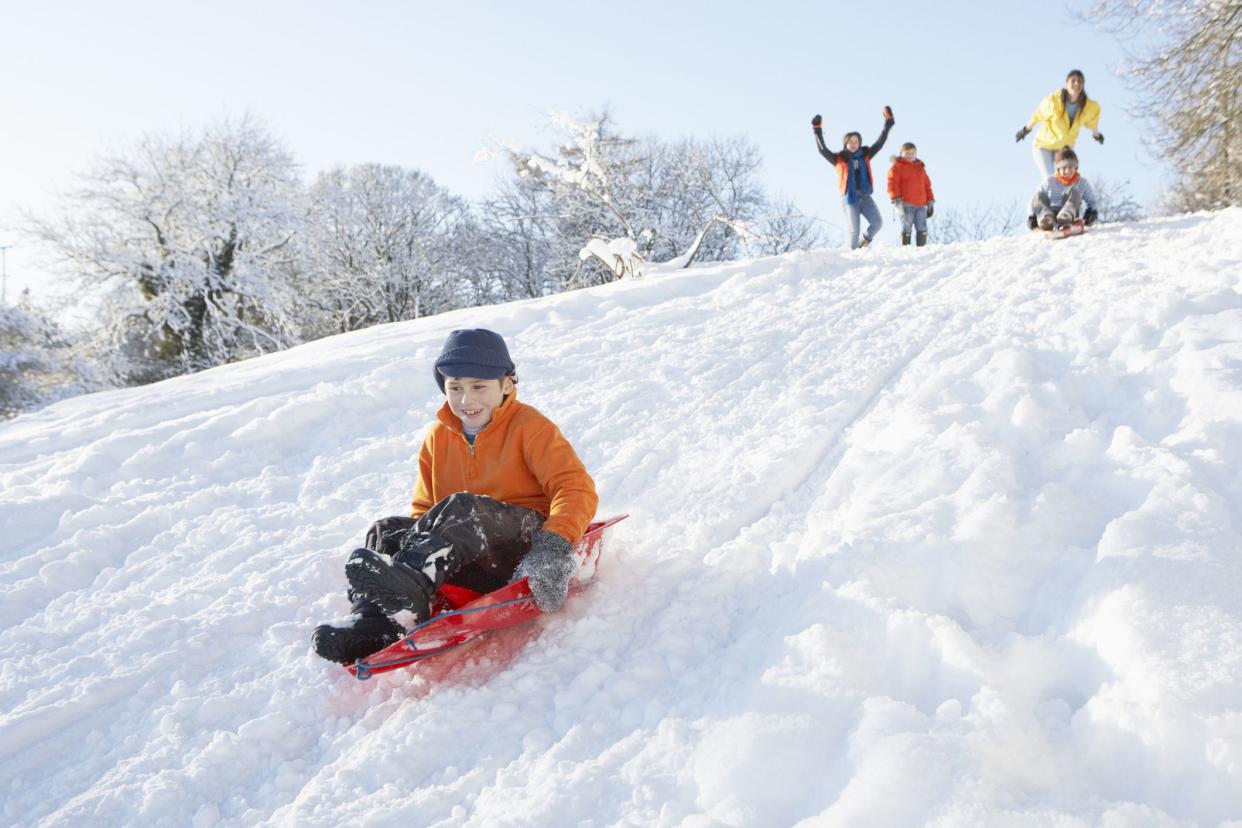 Young Boy Sledging Down Hill With Family Watching And Cheering