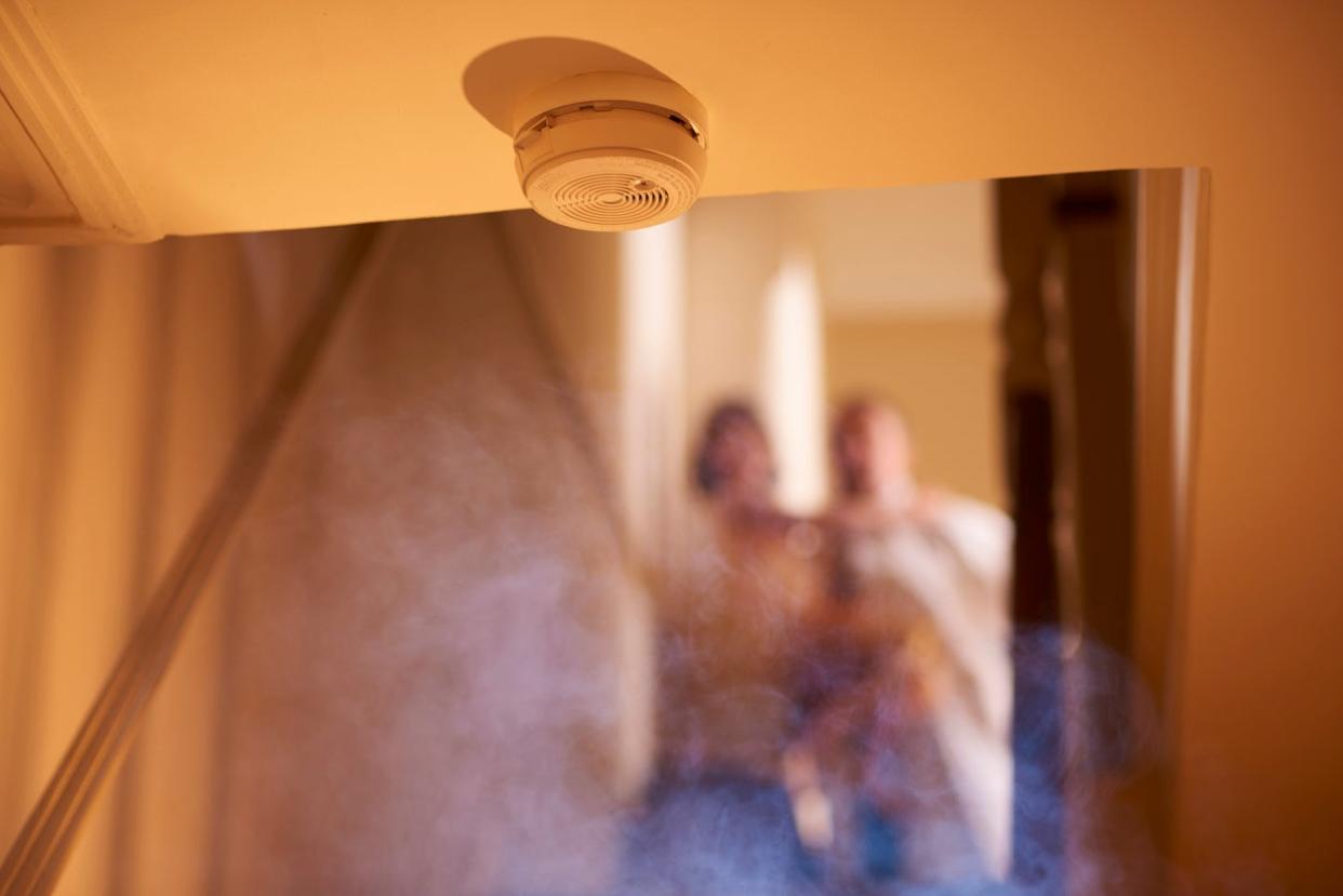 Smoke from downstairs has set the family smoke detector off. Two members of the family can be seen out of focus at the top of the stairs.