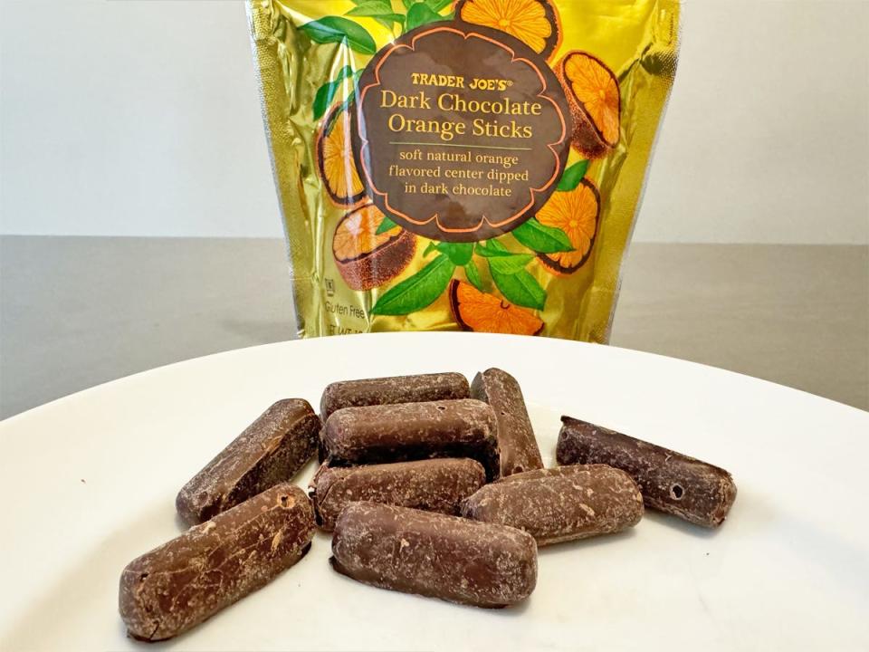 Golden bag with orange fruit graphics and a brown label reading "Trader Joe's dark-chocolate orange sticks with a plate of chocolate candies in front