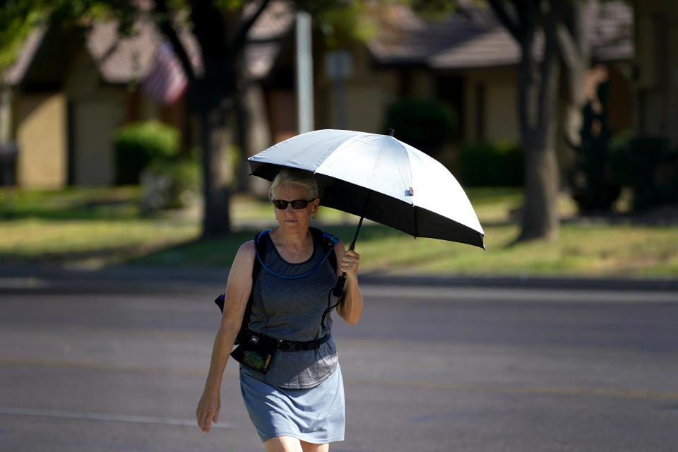 A lady uses an umbrella for shade to combat high temperatures, Monday, July 10, 2023 in Phoenix. National Weather Service says Phoenix has had 10 consecutive days of 110 degrees or above. (AP Photo/Matt York)