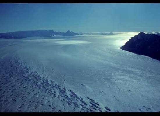 With a width of ten miles, the upper reaches of Scott Glacier spill subtly from the polar plateau, past Mt. Howe, 60 miles to the south, barely seen between the two nunataks (islands in ice) at the horizon.