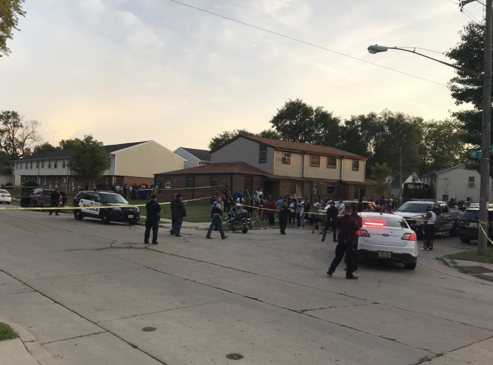 A large group of people can be seen gathering around police cars and tape.