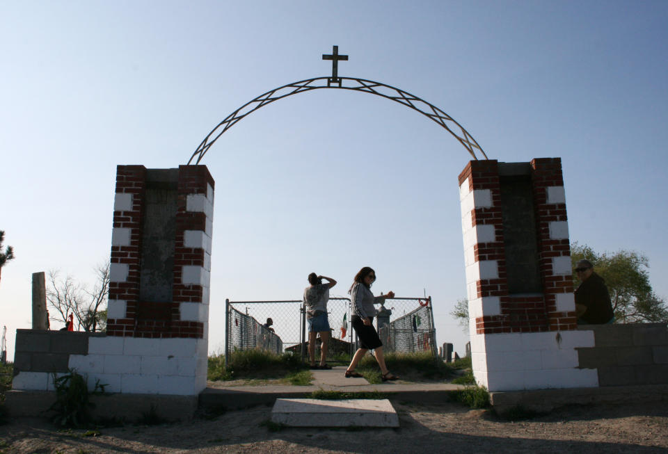 In this May 13, 2012, photo people visit the site of the 1890 Wounded Knee Massacre in Wounded Knee, S.D. The site, located on the Pine Ridge Indian Reservation, which is home to the Oglala Sioux Tribe, is where more than 250 Lakota men, women and children were killed by the 7th Cavalry in 1890. Some tribal members believe the area should be developed into a tourist attraction with a museum. Others, however, are adamantly opposed to development at the site, saying it would be disrespectful since it’s a mass gravesite. (AP Photo/Kristi Eaton)