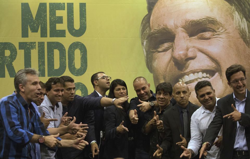 Backdropped by a picture of the presidential candidate Jair Bolsonaro of the right wing Social Liberal Party, recently elected Rio de Janeiro state congressmen, pose for a picture point their fingers like a gun mimicking Bolsonaro, after a press conference in Rio de Janeiro, Brazil, Thursday, Oct. 11, 2018. Bolsonaro will face Workers Party presidential candidate Fernando Haddad in a presidential runoff on Oct. 28. (AP Photo/Leo Correa)