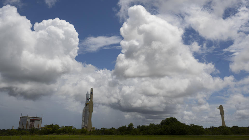 a white ariane 5 rocket rolls out to the launch pad with puffy white clouds above