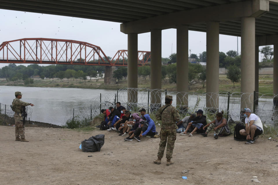 Migrants who had crossed the Rio Grande river into the U.S. are under custody of National Guard members as they await the arrival of U.S. Border Patrol agents in Eagle Pass, Texas, Friday, May 20, 2022. As U.S. officials anxiously waited, many of the migrants crossing the border from Mexico on Friday were oblivious to a pending momentous court ruling on whether to maintain pandemic-related powers that deny a chance to seek asylum on grounds of preventing the spread of COVID-19. (AP Photo/Dario Lopez-Mills)