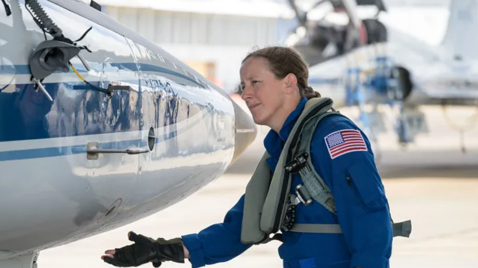 an astronaut in a flight suit reaching for the nose cone of an airplane