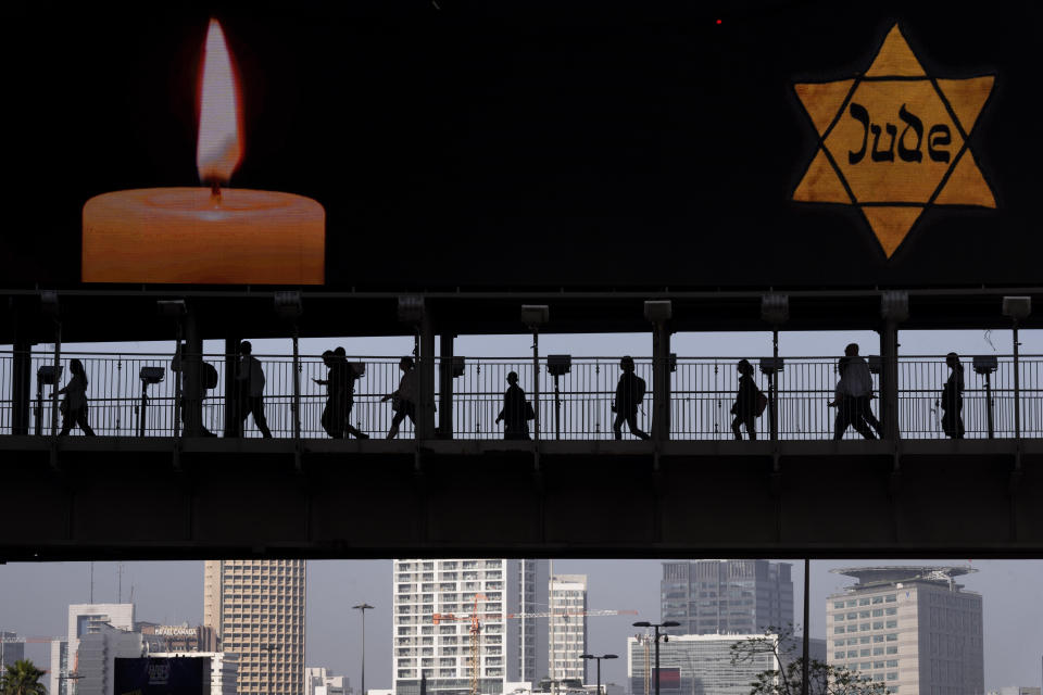 People walk along a bridge lit with a billboard showing a yellow Star of David that reads "Jude", Jew in German, resembling the one Jews were forced to wear in Nazi Germany, during the annual Holocaust Remembrance Day in Ramat Gan, Israel, Tuesday, April 18, 2023. Israel marking the annual Day of Remembrance for the six million Jewish victims of the Nazi genocide who perished during World War II. (AP Photo/Oded Balilty)