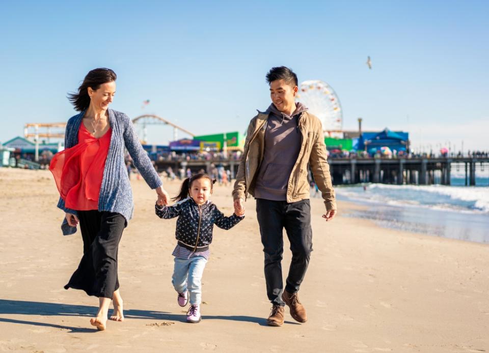 A family holding hands as they walk on Santa Monica beach, with the pier in the background.