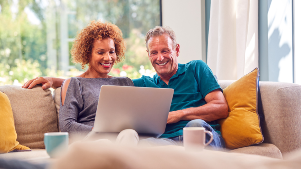 A couple sitting on a couch and smiling at their computer