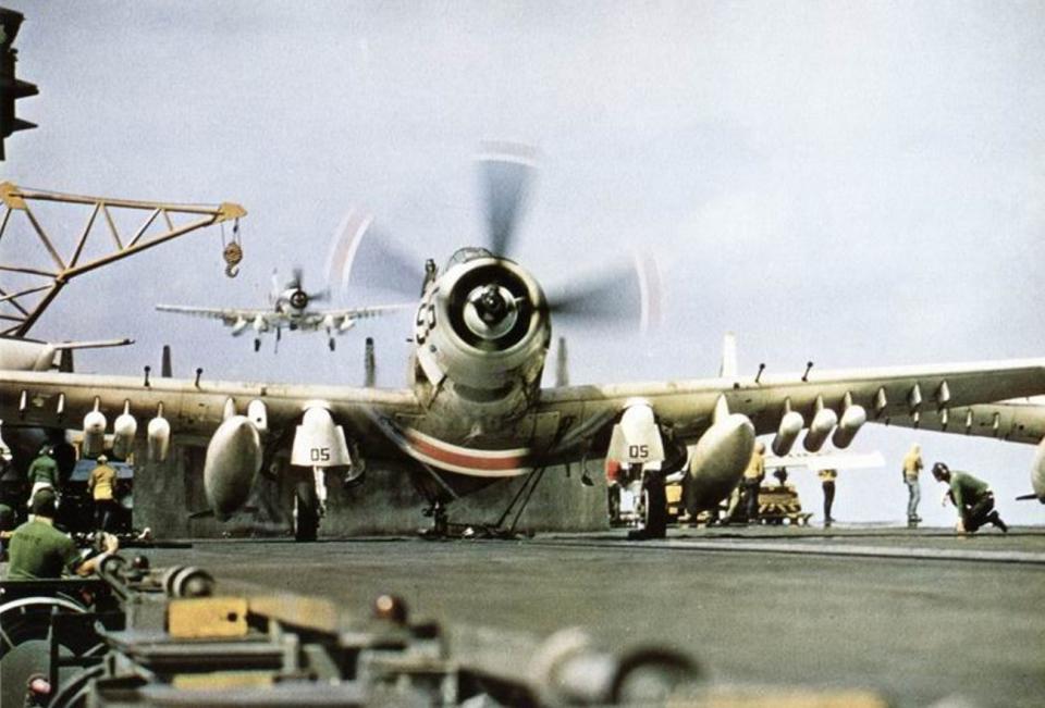 A US Navy A-1H Skyraider with its propellor in motion on the top of an aircraft carrier.