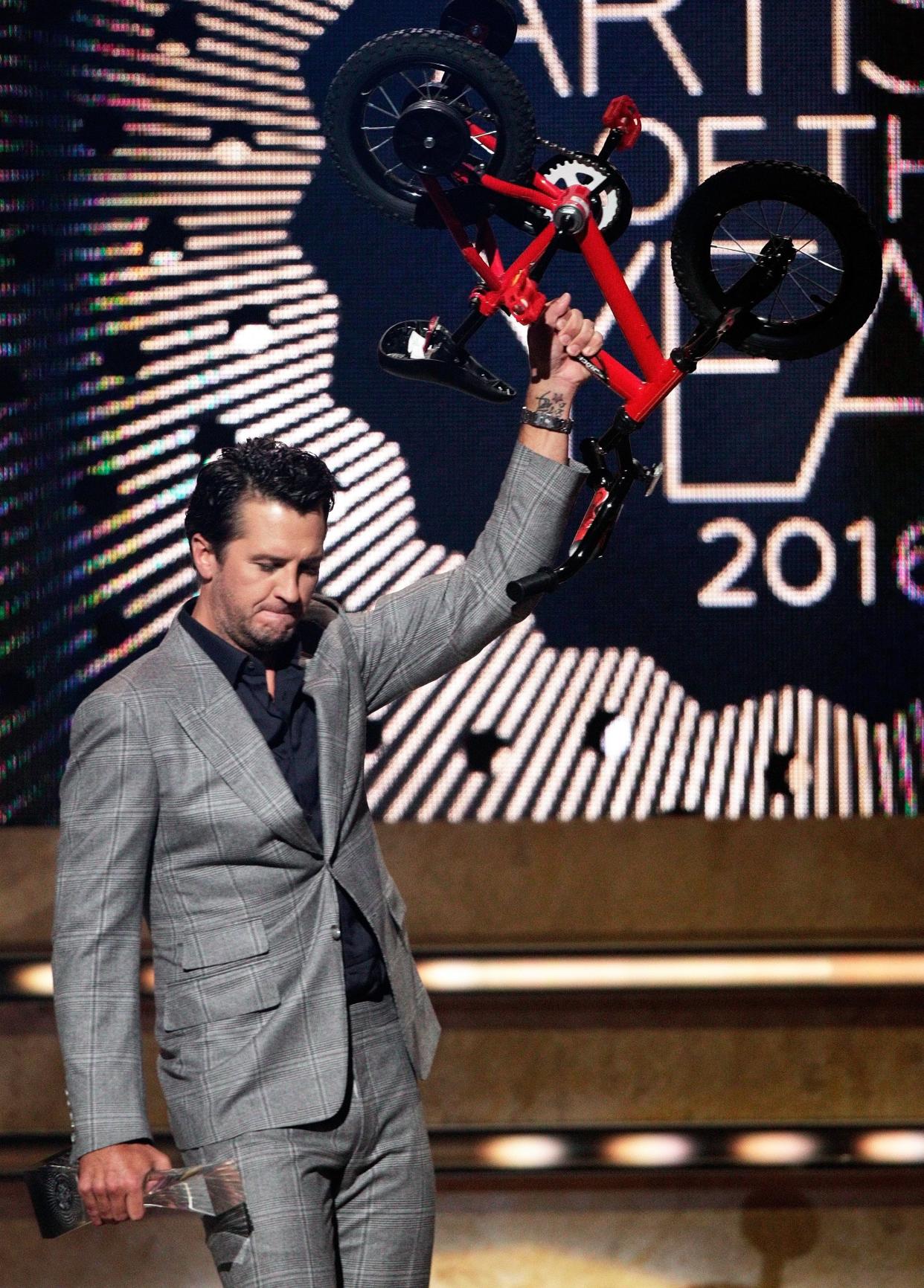 Luke Bryan holds up a small bicycle after being presented the CMT Artists of the Year awards show at the Schermerhorn Symphony Center on Wednesday, Oct. 19, 2016, in Nashville, Tenn. (Photo by Wade Payne/Invision/AP)