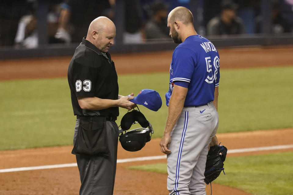 MLB umpire Mike Estabrook (83) inspect the hat of Toronto Blue Jays relief pitcher Tim Mayza (58) during the eighth inning of a baseball game against the Miami Marlins, Wednesday, June 23, 2021, in Miami. (AP Photo/Marta Lavandier)