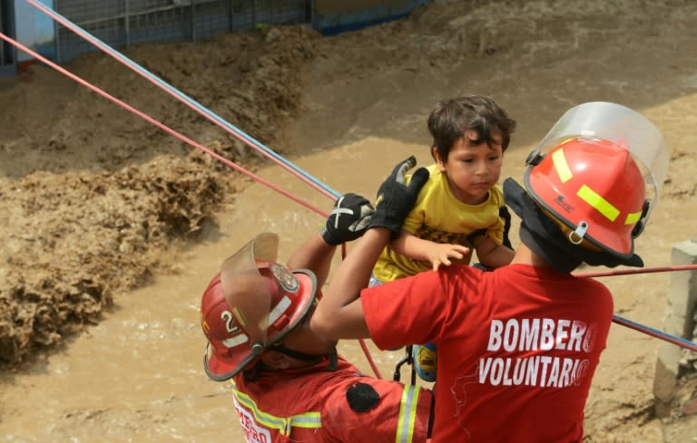 Residents of the Huachipa populous district, east of Lima, are helped on March 17, 2017, by police and firemen rescue teams to cross over flash floods hitting their neighbourhood and isolating its residents